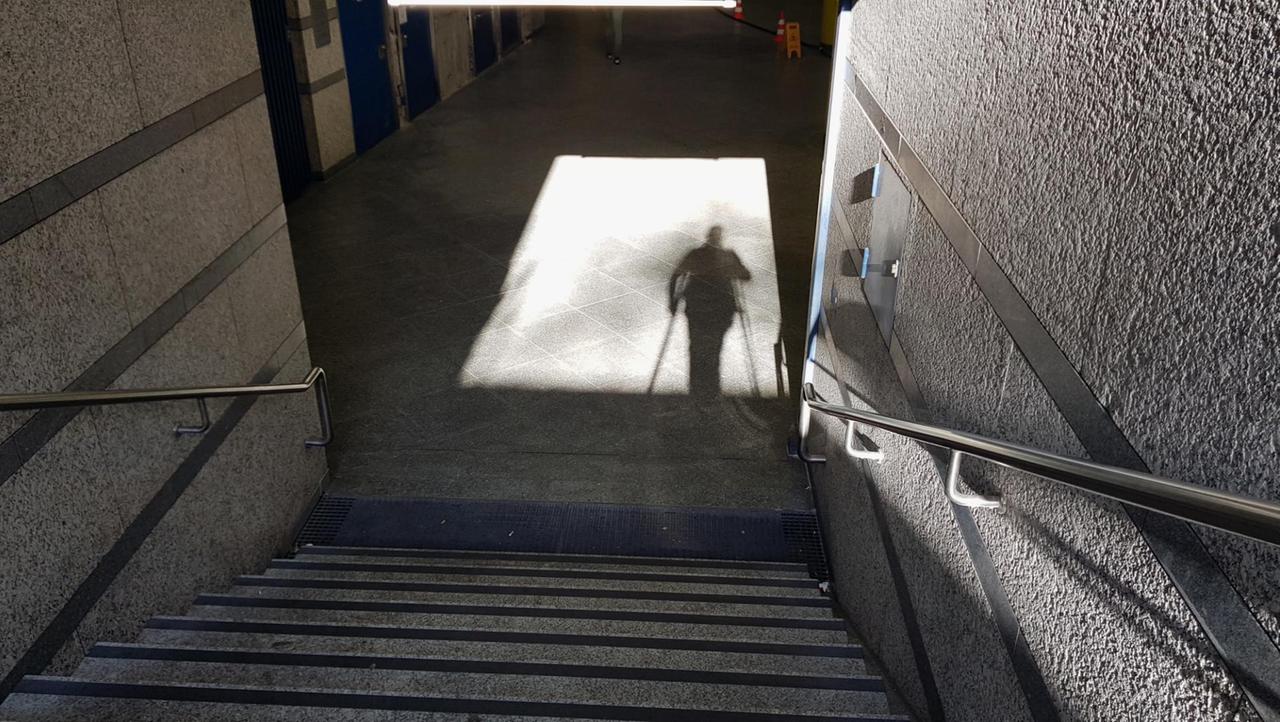 Eine Person steht bei Sonnenschein an einer Treppe und wirft von sich selbst einen Schatten. Eine Person steht bei Sonnenschein an einer Treppe und wirft von sich selbst einen Schatten.