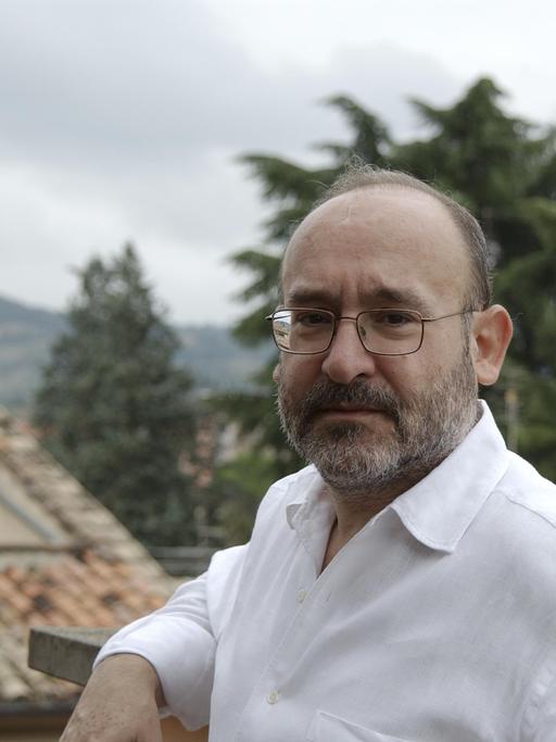 Ein älterer Herr mit Brille steht vor dem Hintergrund von Dächern eines italienischen Dorfes