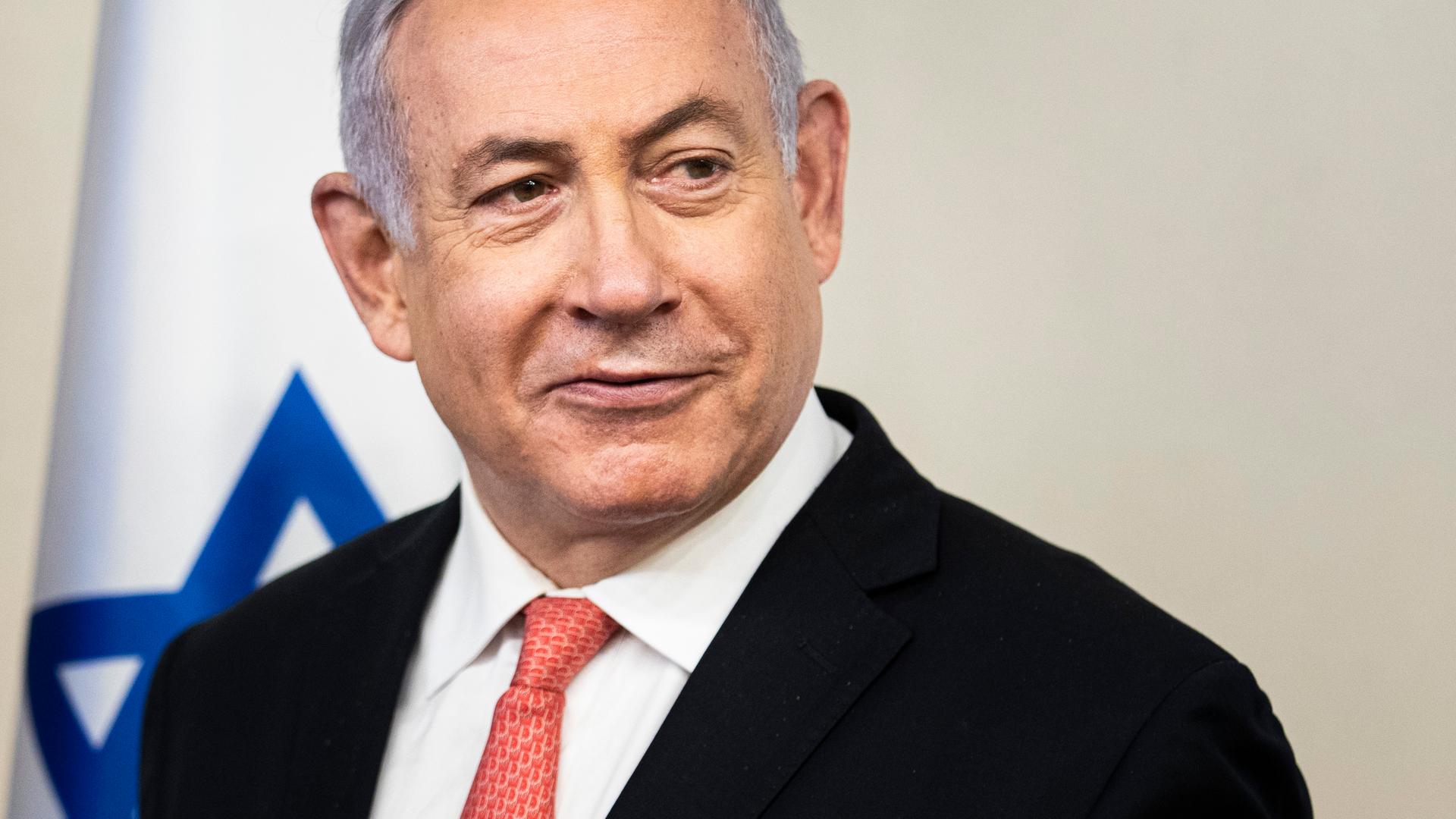 Der israelische Ministerpräsident Benjamin Netanjahu blickt nach rechts aus dem Bild, im Hintergrund ist eine israelische Flagge. Der israelische Ministerpräsident Benjamin Netanjahu blickt nach rechts aus dem Bild, im Hintergrund ist eine israelische Flagge.