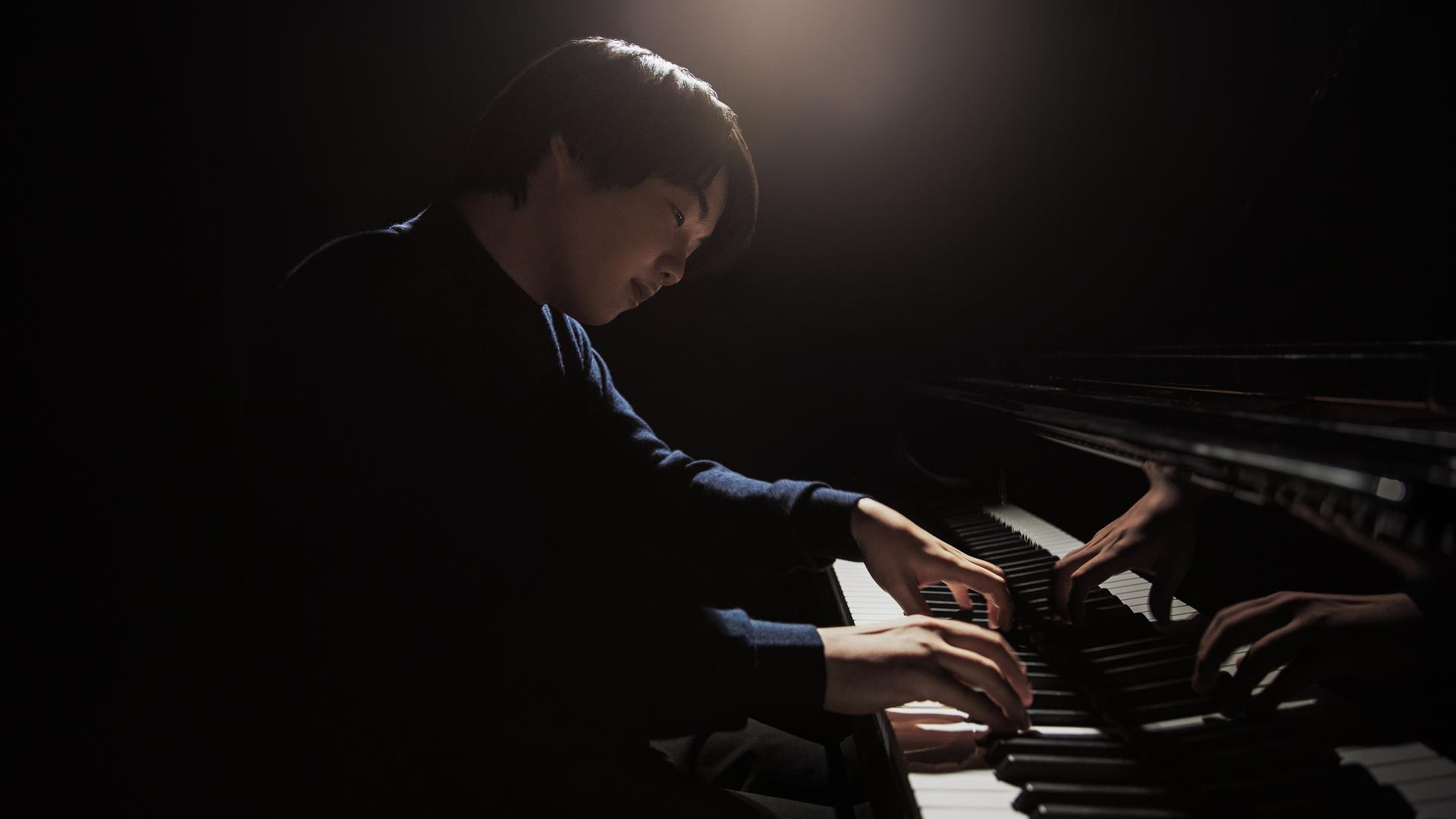 Ein junger japanischer Pianist sitzt an einem Flügel. Er spielt und blickt versonnen auf die Tasten. Ein junger japanischer Pianist sitzt an einem Flügel. Er spielt und blickt versonnen auf die Tasten.