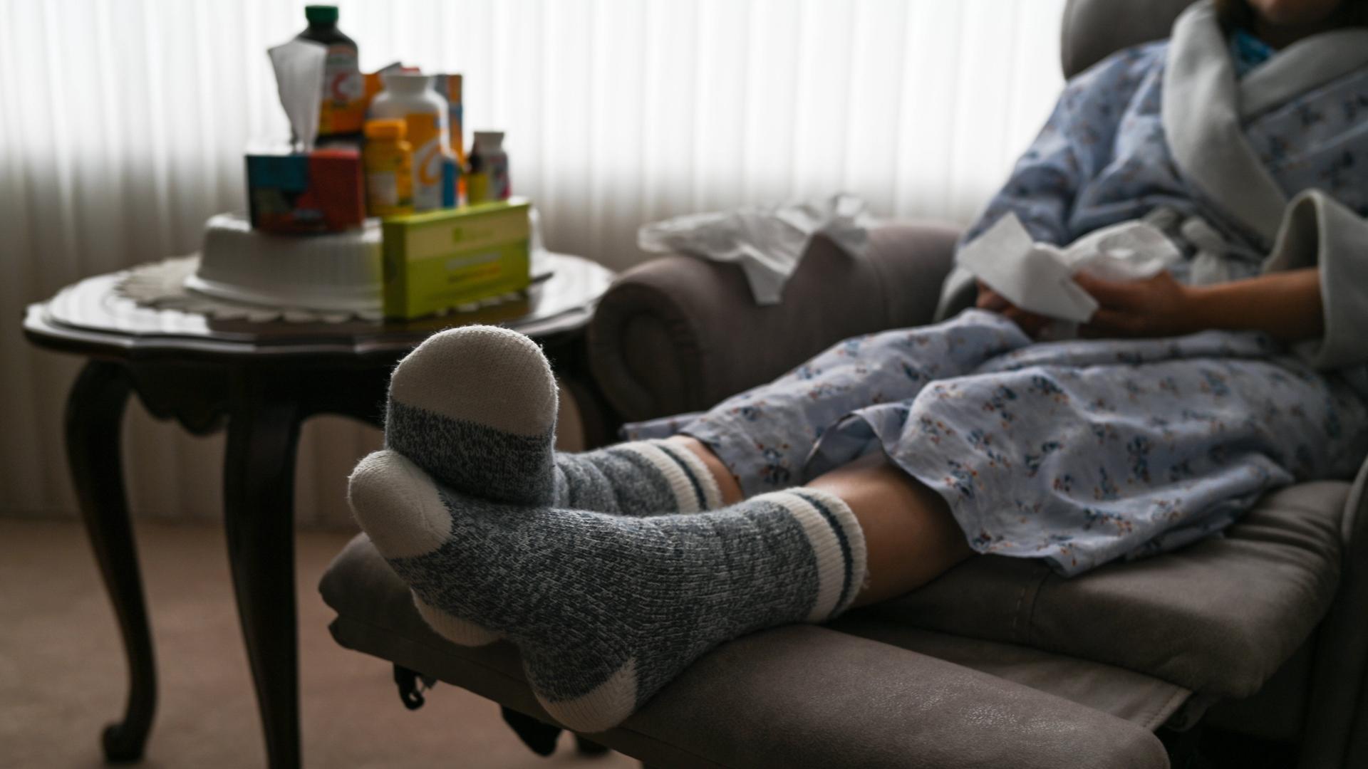 Eine Frau sitzt in Edmonton, Alberta, Kanada, während der Covid-19-Pandemie auf einem Armsessel mit Taschentüchern in der Hand und Medizin auf dem Beistelltisch.