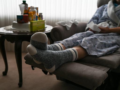 Eine Frau sitzt in Edmonton, Alberta, Kanada, während der Covid-19-Pandemie auf einem Armsessel mit Taschentüchern in der Hand und Medizin auf dem Beistelltisch.
