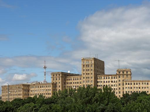 Das langgestreckte Universitätsgebäude von Charkiw erhebt sich über einem grünen Laubwald vor strahlend blauem Himmel. Das langgestreckte Universitätsgebäude von Charkiw erhebt sich über einem grünen Laubwald vor strahlend blauem Himmel.