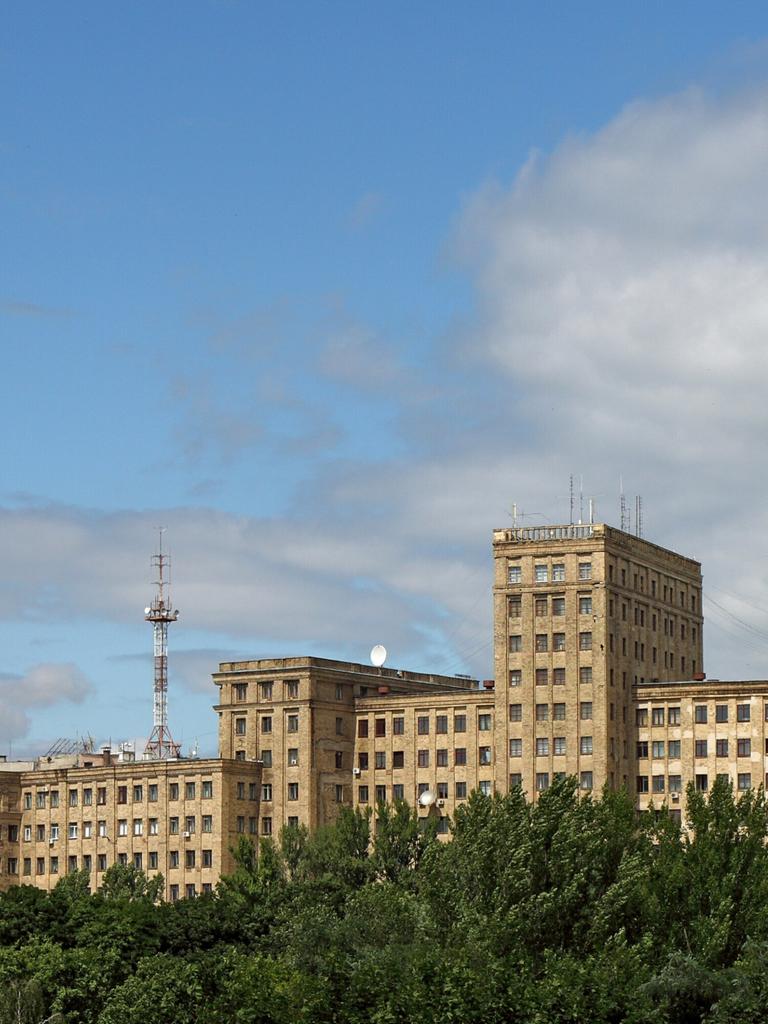 Das langgestreckte Universitätsgebäude von Charkiw erhebt sich über einem grünen Laubwald vor strahlend blauem Himmel. Das langgestreckte Universitätsgebäude von Charkiw erhebt sich über einem grünen Laubwald vor strahlend blauem Himmel.