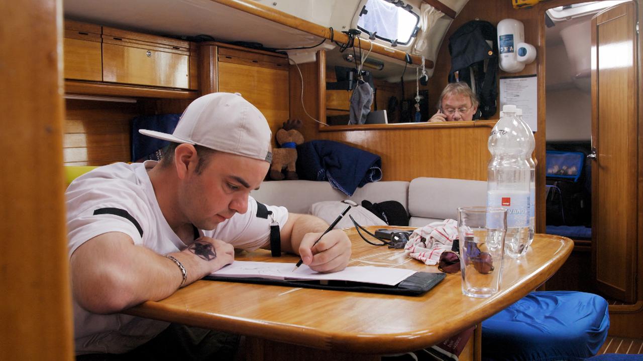 Ein junger Mann mit Baseballkappe beugt sich mit einem Bleistift in der Hand über einen Zeichenblock. Ein junger Mann mit Baseballkappe beugt sich mit einem Bleistift in der Hand über einen Zeichenblock.