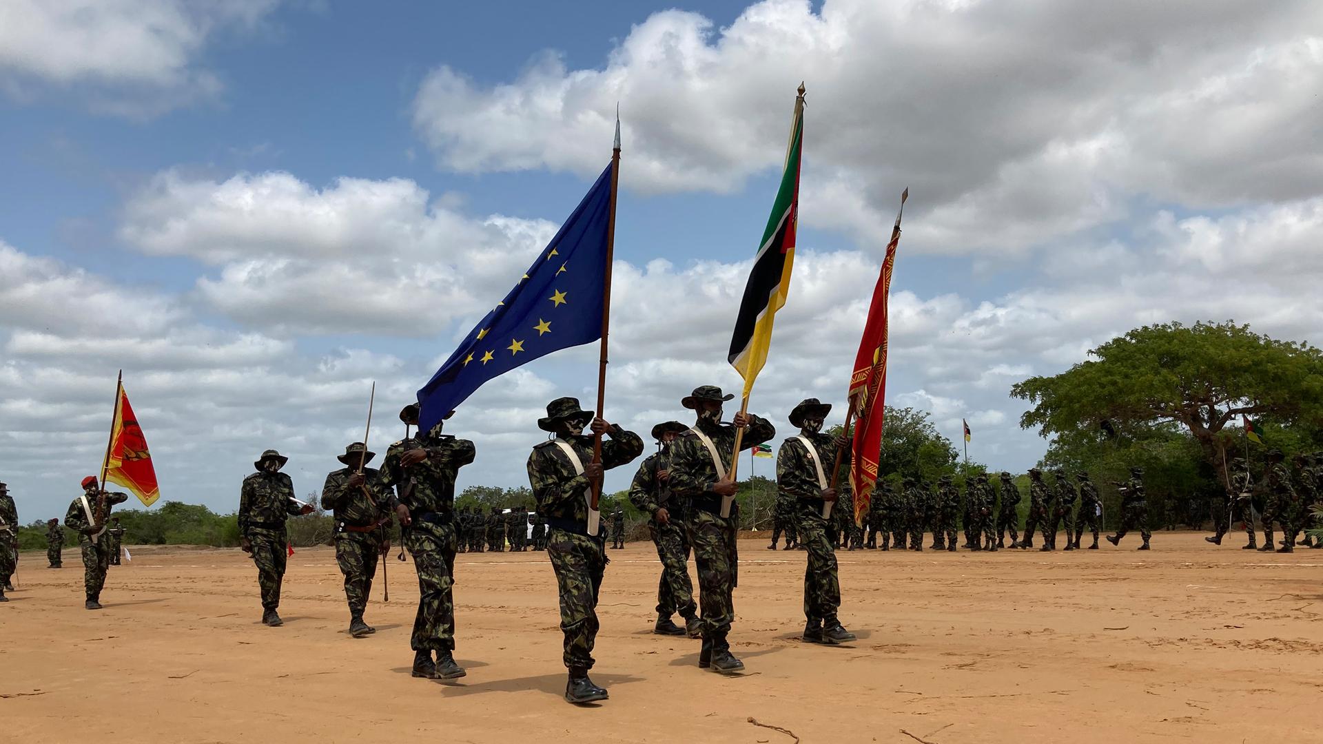 Mosambikanische Soldaten sind zu einer Formation aufgestellt und präsentieren Fahnen, darunter auch die der EU.