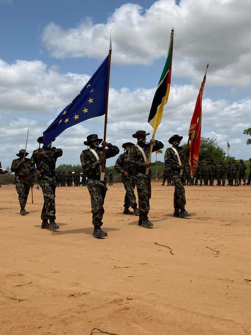 Mosambikanische Soldaten sind zu einer Formation aufgestellt und präsentieren Fahnen, darunter auch die der EU.