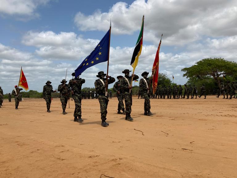 Mosambikanische Soldaten sind zu einer Formation aufgestellt und präsentieren Fahnen, darunter auch die der EU.