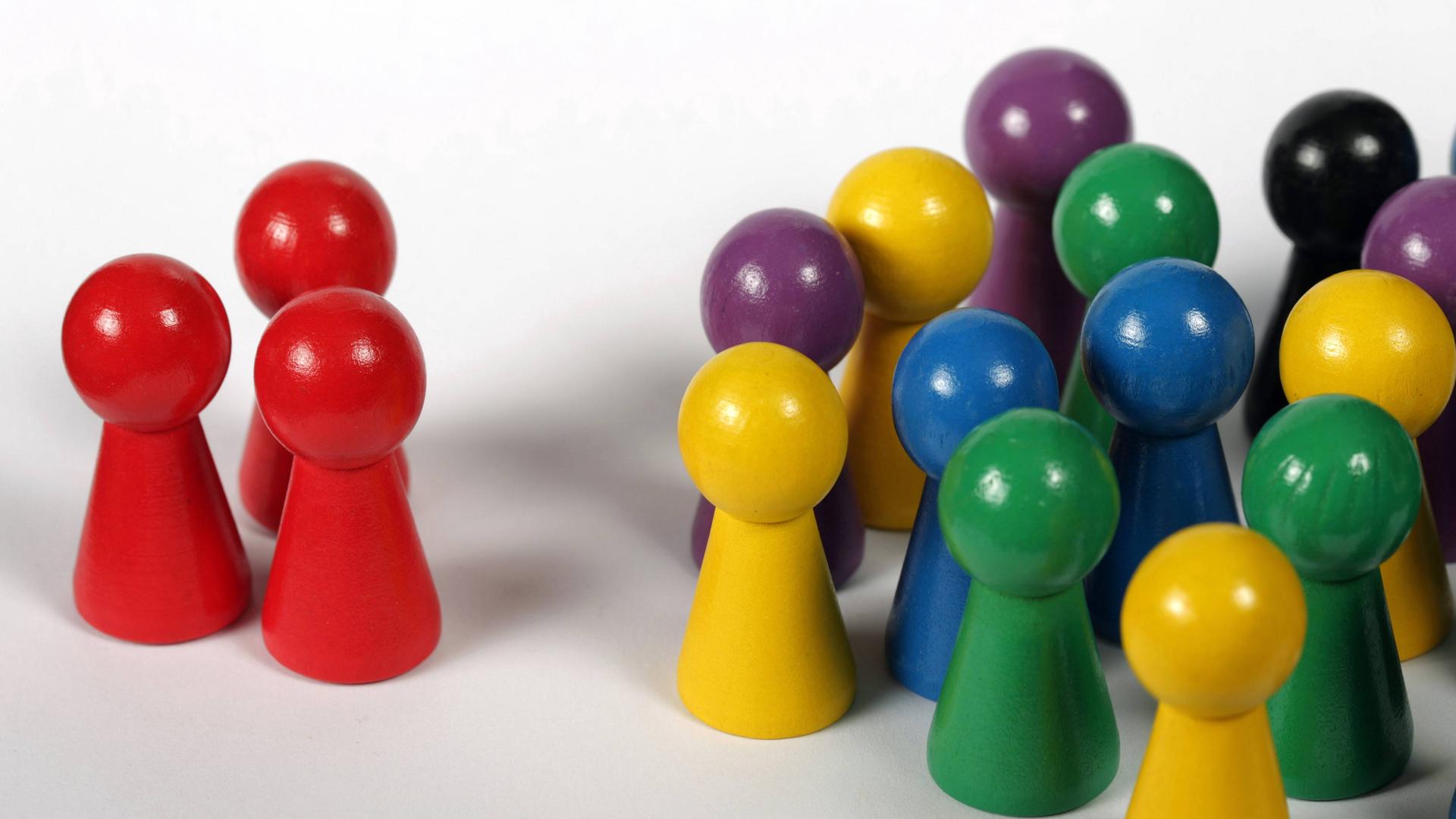 Eine bunte Anzahl von Spielfiguren steht drei roten, seperierten gegenüber. Eine bunte Anzahl von Spielfiguren steht drei roten, seperierten gegenüber.