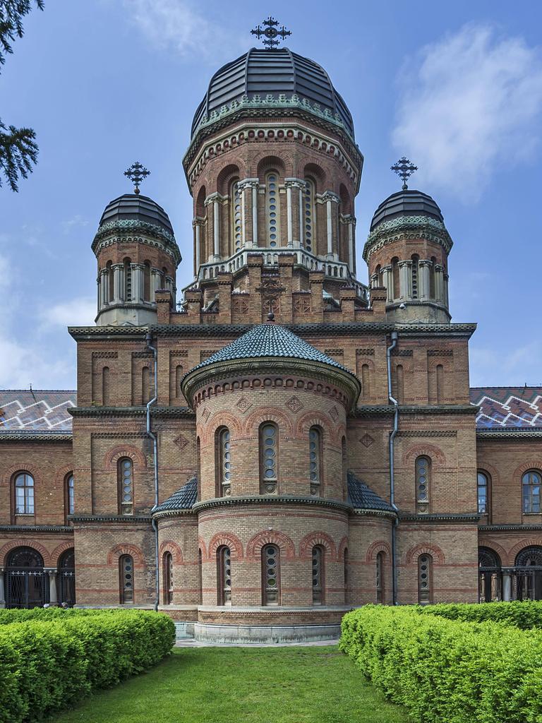 Ein Ziegelbau mit Türmen und Kuppeln steht in einem Park mit akkurat geschnittenen Hecken, die den Blick auf das Gebäude lenken. Ein Ziegelbau mit Türmen und Kuppeln steht in einem Park mit akkurat geschnittenen Hecken, die den Blick auf das Gebäude lenken.