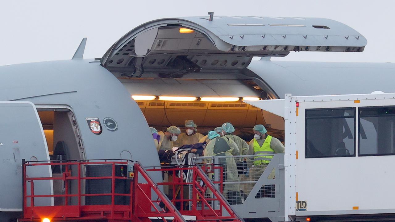 Mehrere Helfer in medizinischer Schutzkleidung schieben einen schwer kranken Patienten auf einer Liege in ein Flugzeug. Mehrere Helfer in medizinischer Schutzkleidung schieben einen schwer kranken Patienten auf einer Liege in ein Flugzeug.