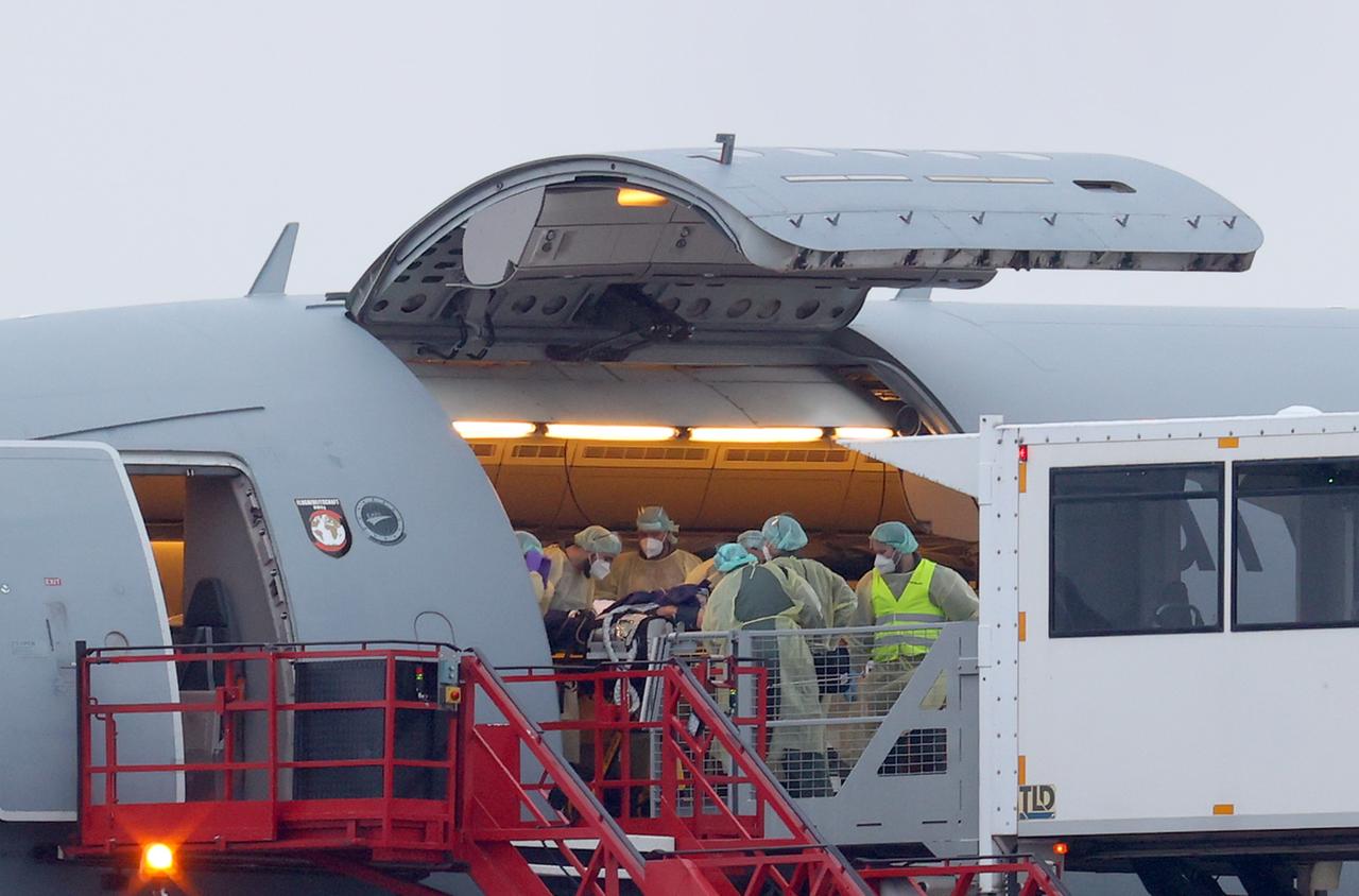 Mehrere Helfer in medizinischer Schutzkleidung schieben einen schwer kranken Patienten auf einer Liege in ein Flugzeug. Mehrere Helfer in medizinischer Schutzkleidung schieben einen schwer kranken Patienten auf einer Liege in ein Flugzeug.