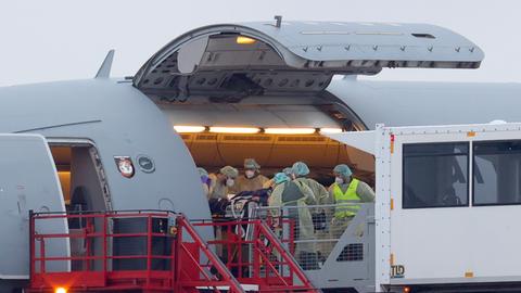 Mehrere Helfer in medizinischer Schutzkleidung schieben einen schwer kranken Patienten auf einer Liege in ein Flugzeug.