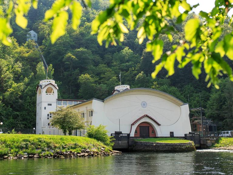 Das weiße, historische Gebäude, das einer Kirche mit Turm gleicht, spiegelt sich im Flusswasser.