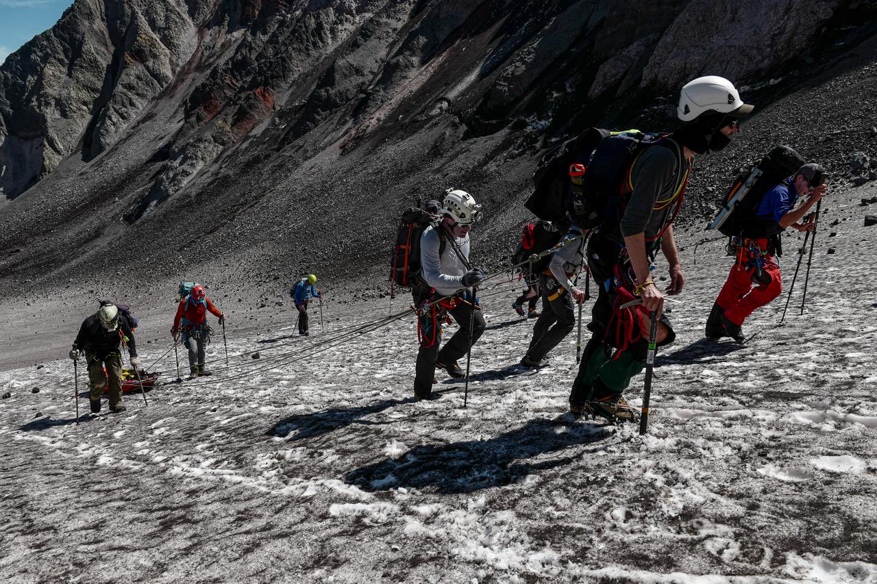Menschen mit Bergsteigerausrüstung und Stöcken gehen einen schneebedeckten Hang hinauf. Menschen mit Bergsteigerausrüstung und Stöcken gehen einen schneebedeckten Hang hinauf.