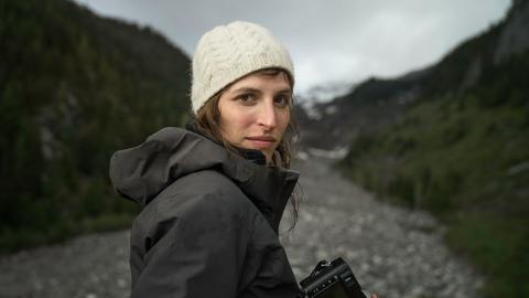 Porträt der Journalistin und Aktivistin Theresa Breuer in der Natur in Regenjacke mit Kamera in der Hand.