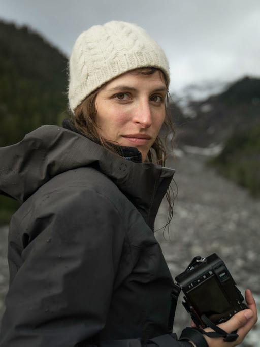 Porträt der Journalistin und Aktivistin Theresa Breuer in der Natur in Regenjacke mit Kamera in der Hand.