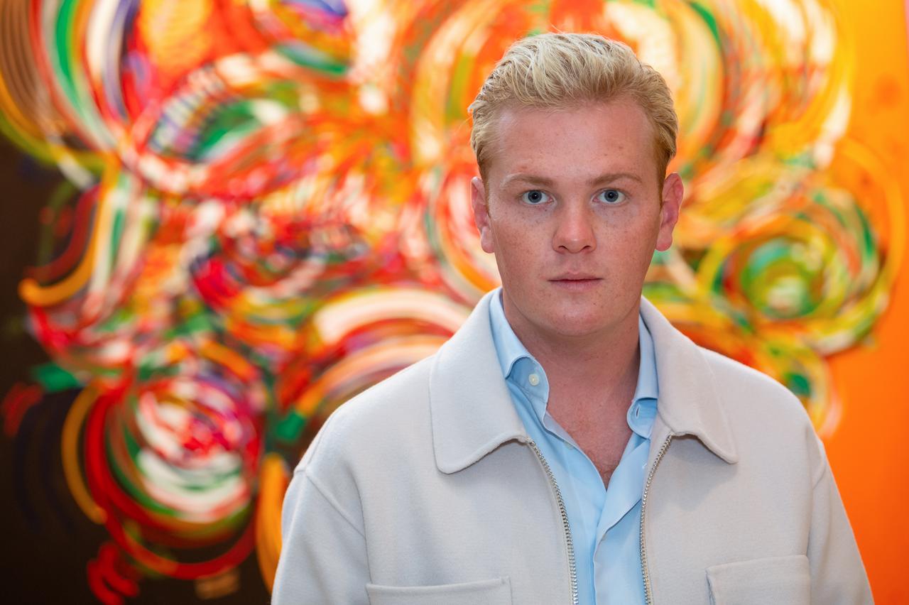 Leon Löwentraut. Ein junger Mann mit kurzen blonden Haaren steht vor einem Bild. Leon Löwentraut. Ein junger Mann mit kurzen blonden Haaren steht vor einem Bild.