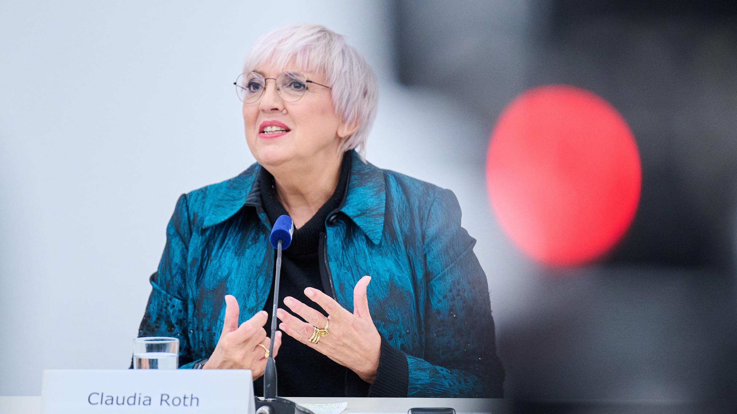 Claudia Roth. Eine ältere Frau mit kurzen hellen Haaren und Brille steht an einem Pult und hält eine Rede.