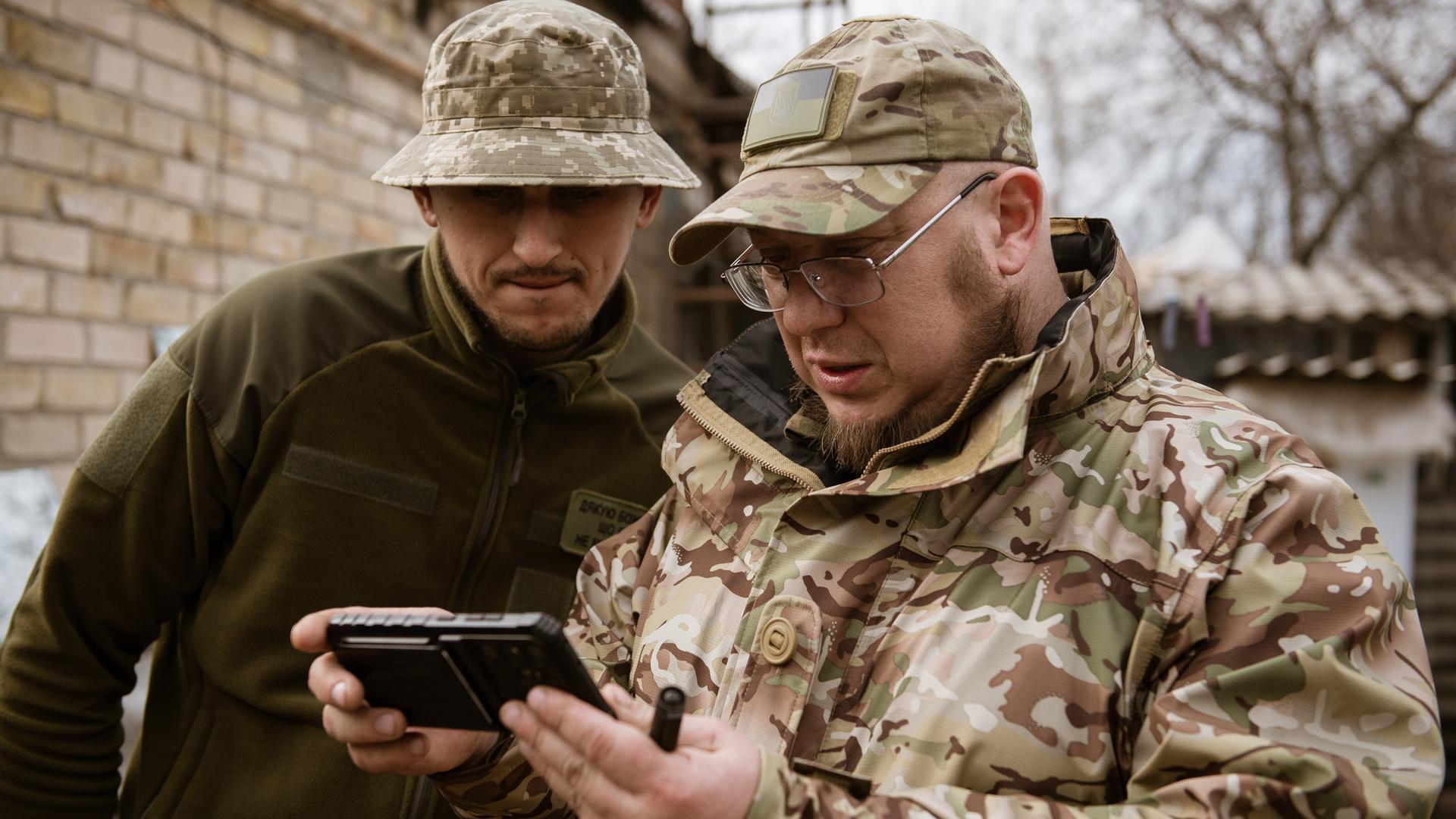 Zwei ukrainische Soldaten betrachten ein Handyvideo von Drohnenangriffen. Zwei ukrainische Soldaten betrachten ein Handyvideo von Drohnenangriffen.