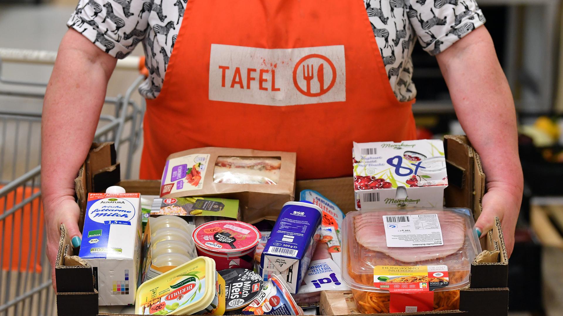 Eine Person mit Tafeln-Schürze und einem Karton voller Lebensmittel Eine Person mit Tafeln-Schürze und einem Karton voller Lebensmittel
