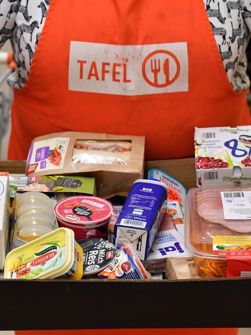 Eine Person mit Tafeln-Schürze und einem Karton voller Lebensmittel