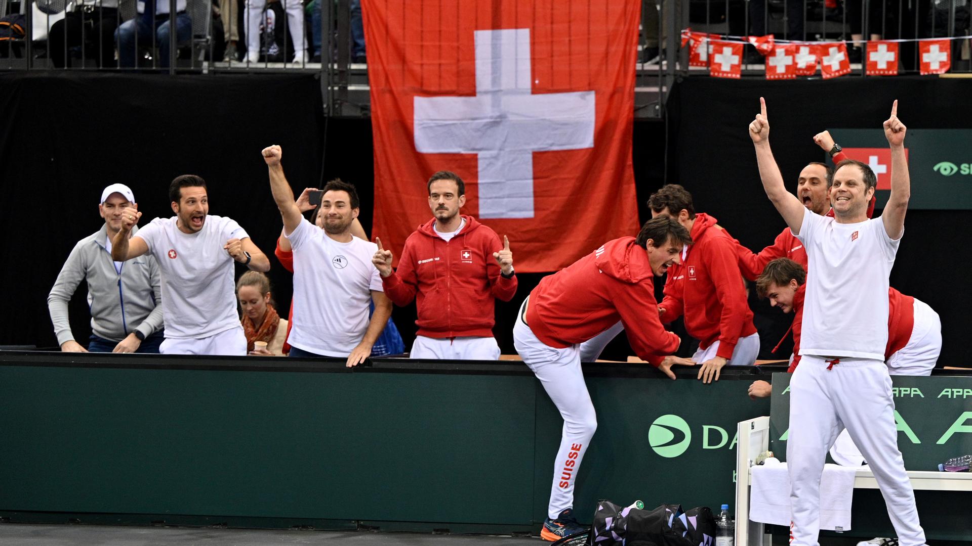 Die Schweizer Tennis-Spieler jubeln am Seitenrand des Spielfelds. Im Hintergrund ist eine schweizerische Flagge zu sehen.