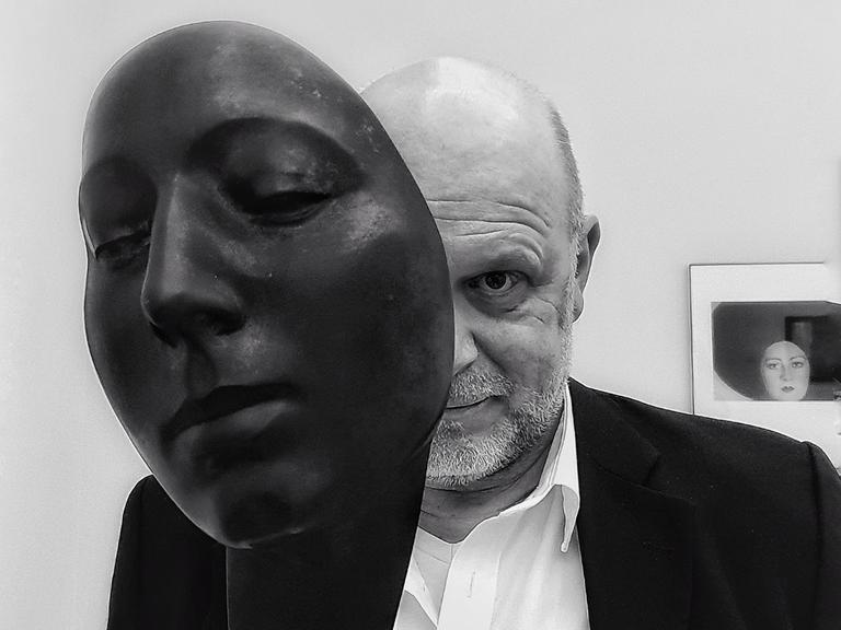 Der Fotokünstler Gregor Wildförster schaut hinter der Skulptur eines Gesichtes hervor. Sein Gesicht ist auf der Schwarz-Weiß-Fotografie dabei nur zur Hälfte zu sehen. 