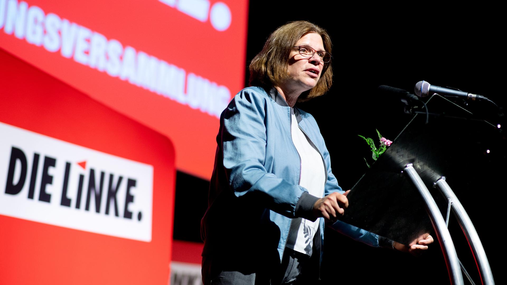 Eine Frau mit länglichen Haaren und Brille steht auf einer Bühne vor einem Pult und hält eine Rede.