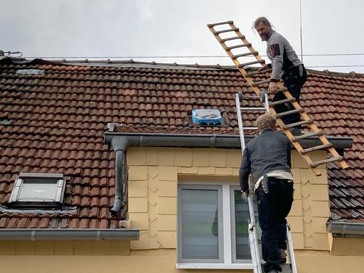Zwei Dackdecker steigen auf ein Hausdach hinauf, um es zu reparieren. 