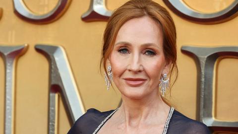 J.K. Rowling blickt bei einem Fototermin in die Kamera. Die Mittfünfzigerin mit rötlichen Haaren trägt ein blaues Kleid und Brilliantohrringe.