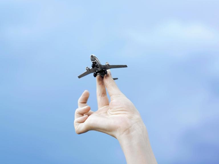 Eine Hand hält ein Modellflugzeug vor blauem Himmel.