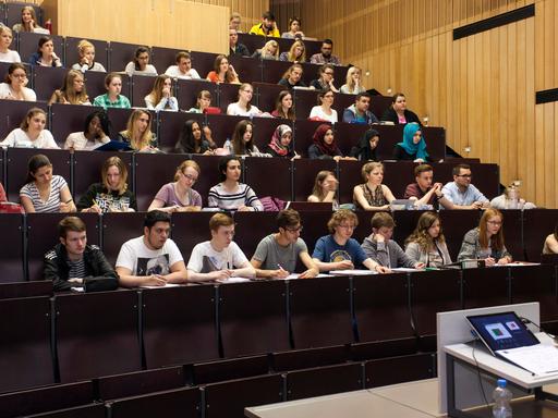 Junge Männer und Frauen in einem Universitätshörsaal. Sie sitzen in mehreren, steil ansteigenden Reihen hintereinander. Es handelt sich um Studierende der Universität Düsseldorf.