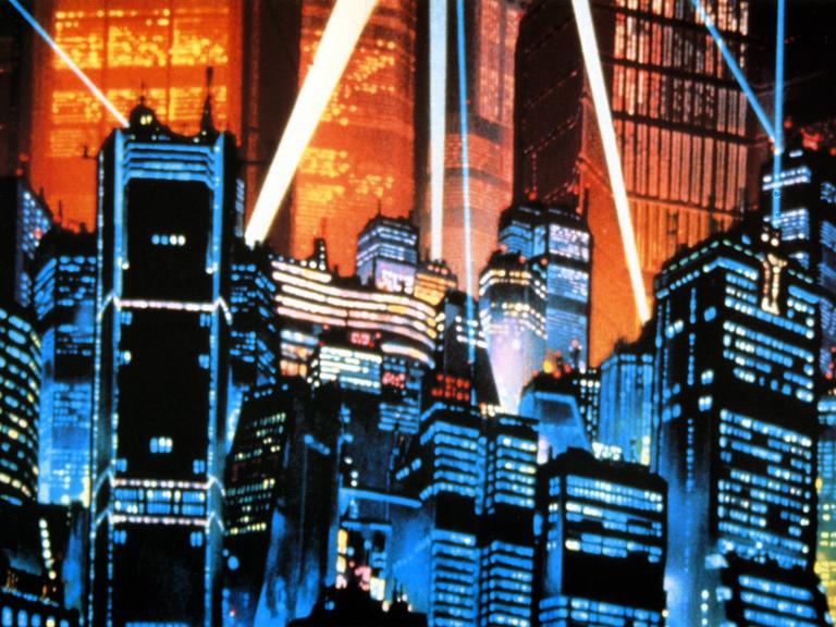 Eine Aufnahme aus dem Anime-Film Akria aus dem Jahr 1988. Es ist die von Scheinwerfern angeleuchtete Skyline der Stadt Neo-Tokyo mit vielen Hochäusern.
