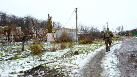 Schnee liegt im ukrainischen Örtchen Rubizhne auf der Wiese, ein Soldat läuft über einen Weg