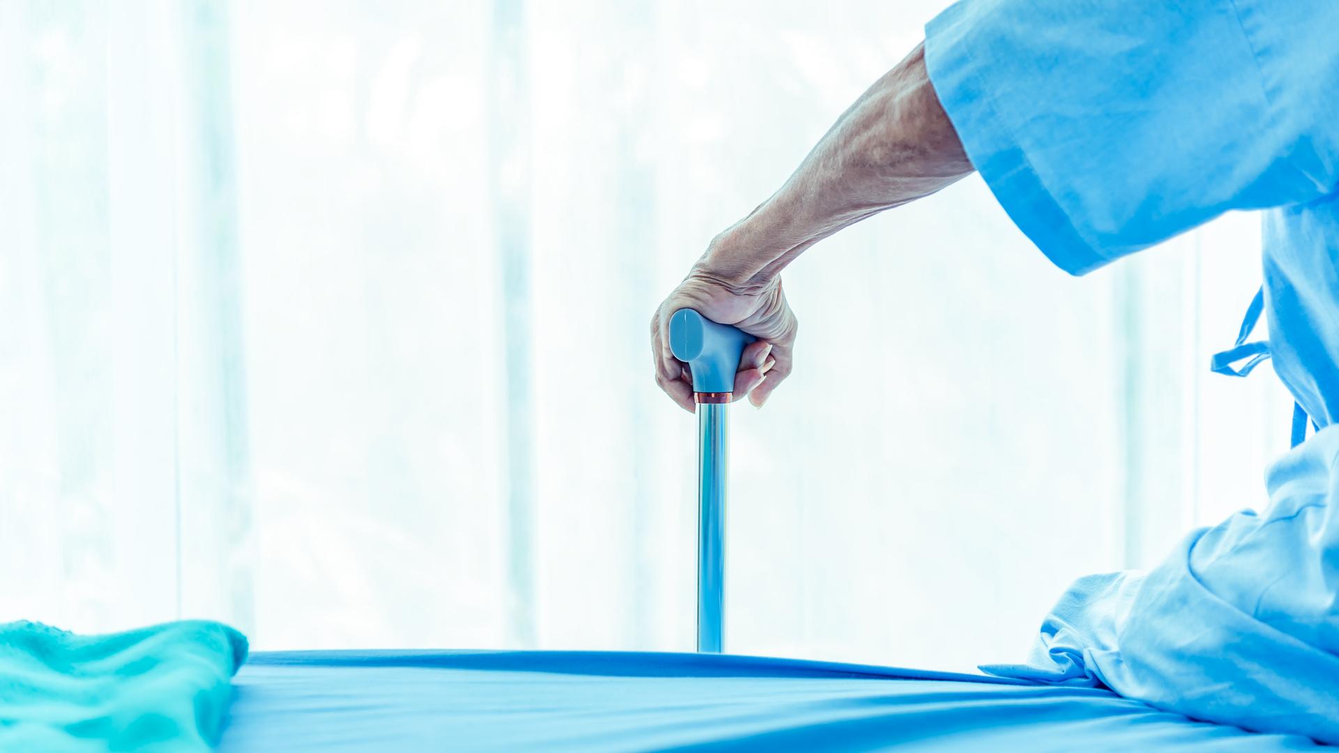 Ein Mensch in blauer Krankenhausbekleidung stützt sich auf einen blauen Gehstock. Ein Mensch in blauer Krankenhausbekleidung stützt sich auf einen blauen Gehstock.
