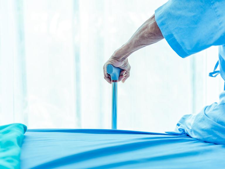 Ein Mensch in blauer Krankenhausbekleidung stützt sich auf einen blauen Gehstock.