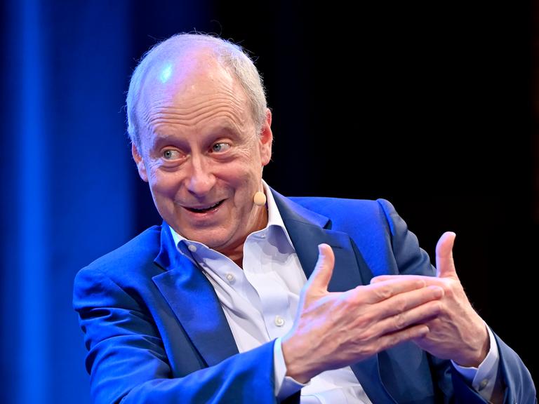 Der Philosoph Michael J. Sandel bei einem Gespräch. Er trägt einen blauen Anzug und ein weißes Hemd.