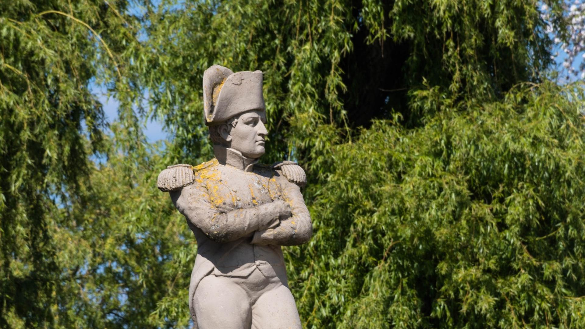 Ein steinernes Monument zeigt Napoleon mit verschränkten Armen in Uniform, während er seine Arme verschränkt.