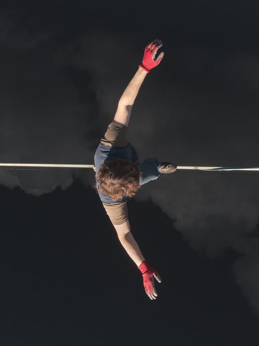 Ein Seiltänzer von (oben fotografiert) läuft auf einem Seil über Wolken. 