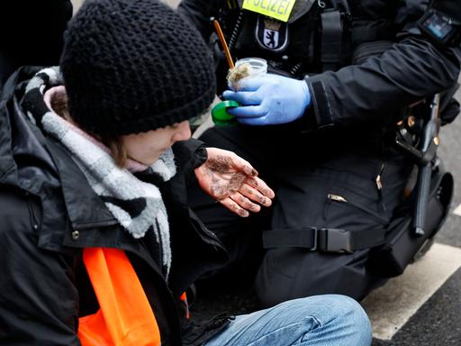 Eine junge Aktivistin der Letzten Generation hat sich in Berlin auf einer Straße festgeklebt, ihre Hände zeigen die Sekundenkleberspuren, nachdem ein Polizist sie losgemacht hat.