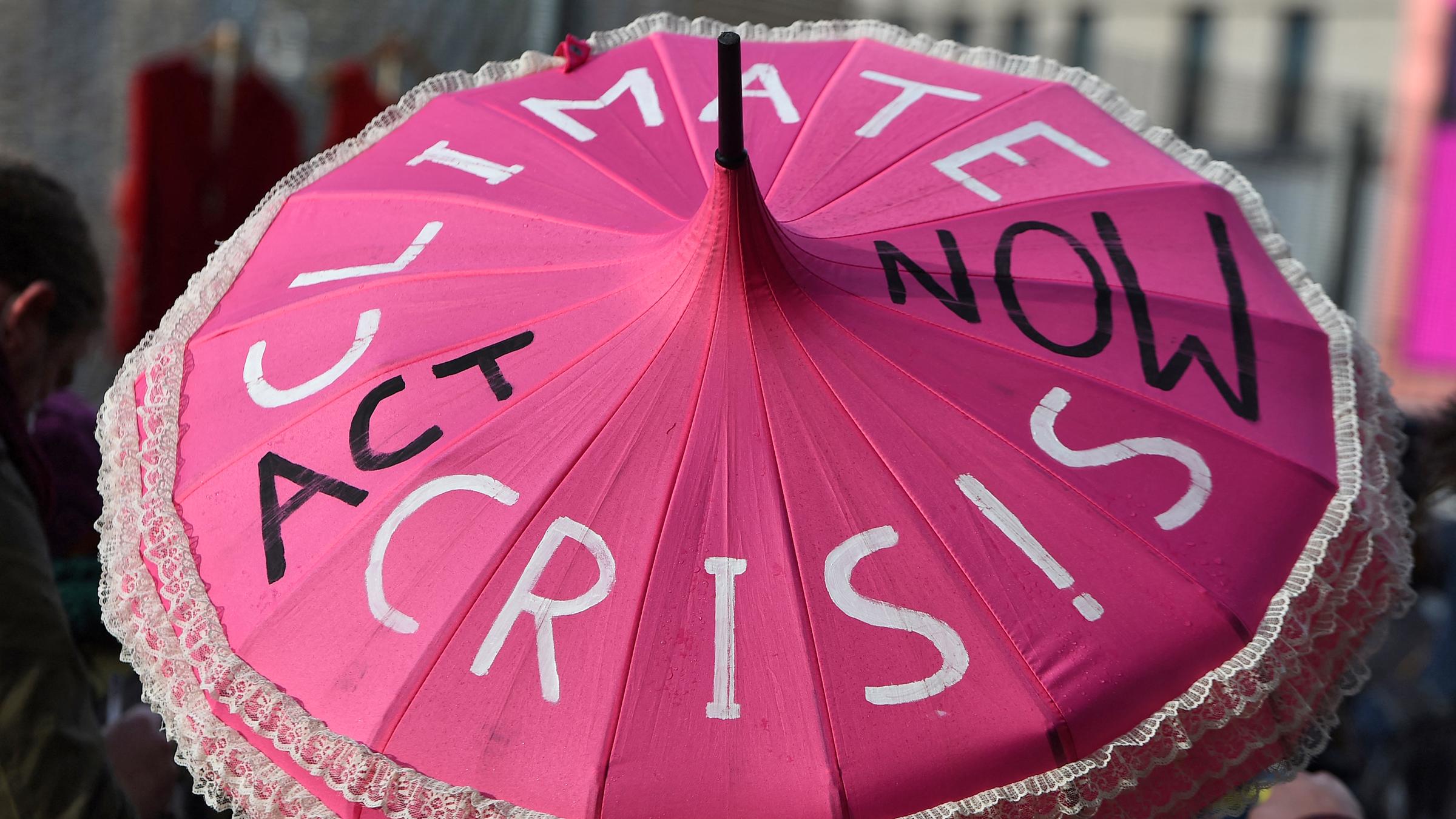 Rosa Schirm eines Klimaaktivisten mit der Aufschrift "Climate crisis act now".