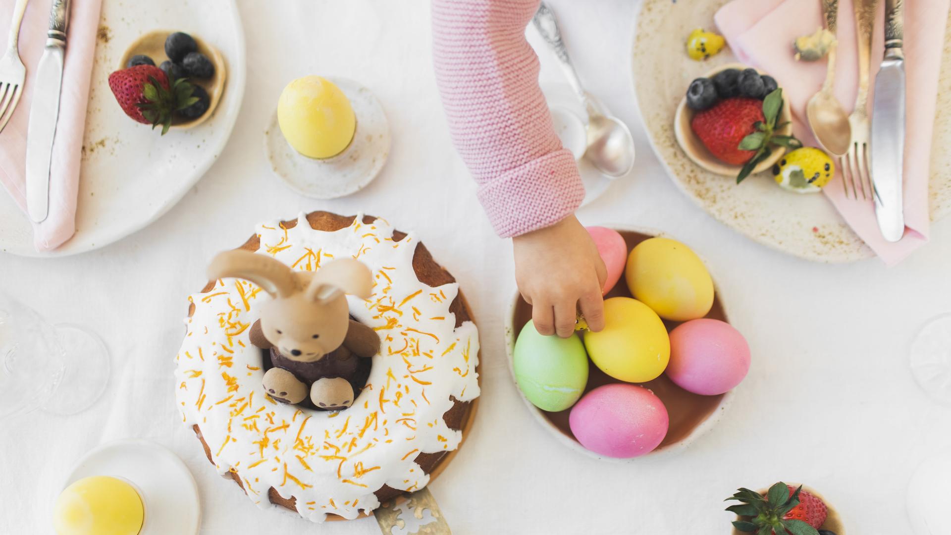 Ein für Ostern gedeckter und dekorierter Frühstückstisch. Eine kleine Kinderhand greift nach einem Ei. Ein für Ostern gedeckter und dekorierter Frühstückstisch. Eine kleine Kinderhand greift nach einem Ei.