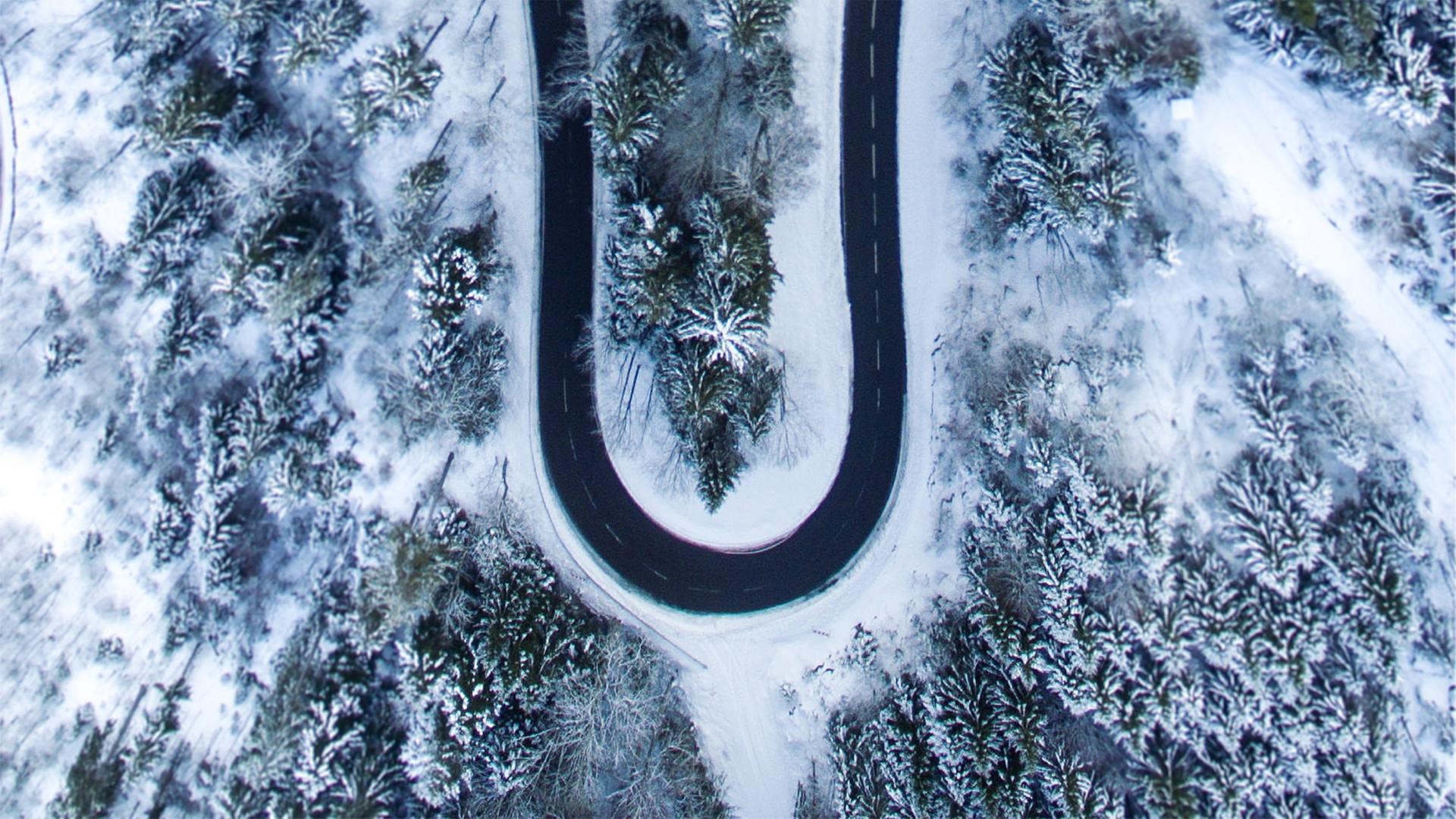 Eine sich schlängelnde Straße in verschneiter Waldlandschaft aus der Vogelperspektive. Eine sich schlängelnde Straße in verschneiter Waldlandschaft aus der Vogelperspektive.