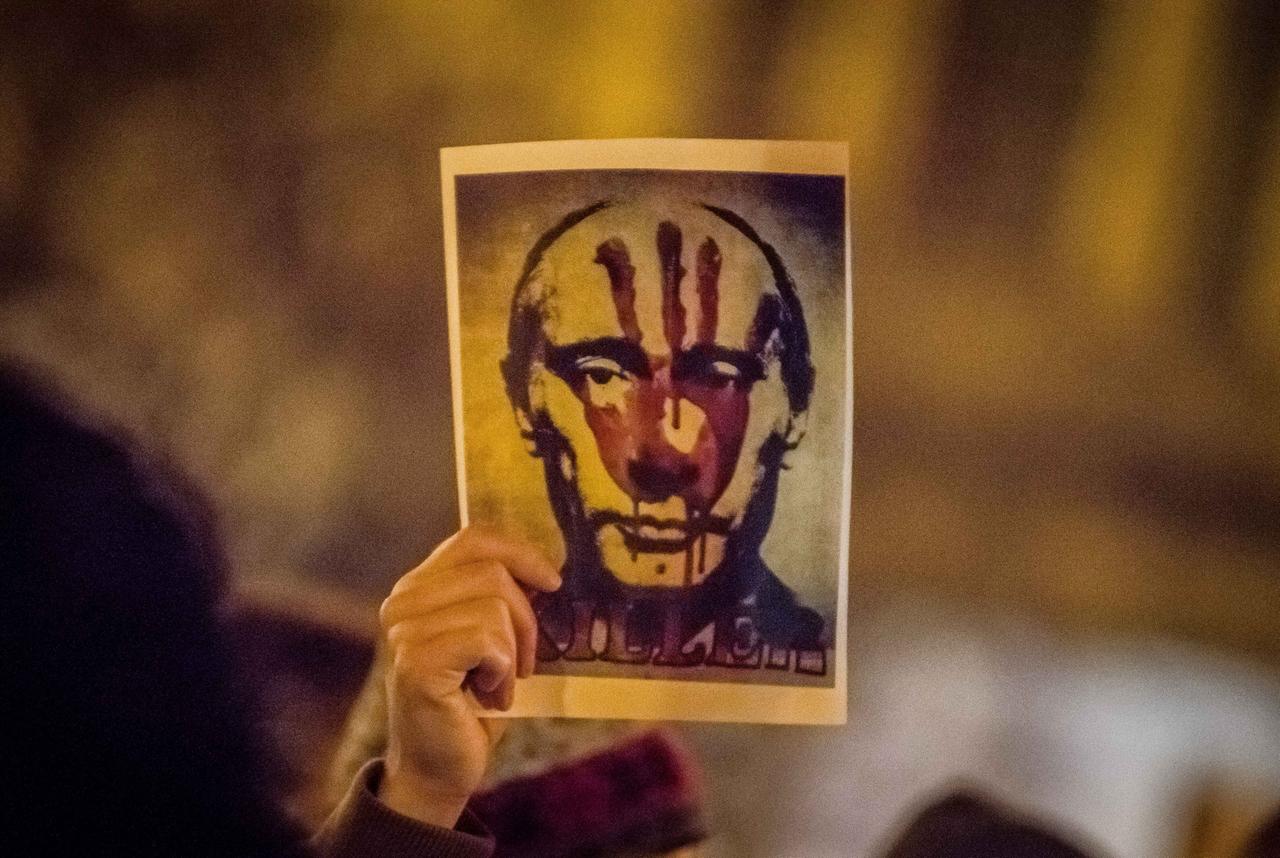 Eine Hand hält ein Bild von Putin hoch, auf dem ein blutiger Handabdruck und die Aufschrift "Killer" zu sehen ist.