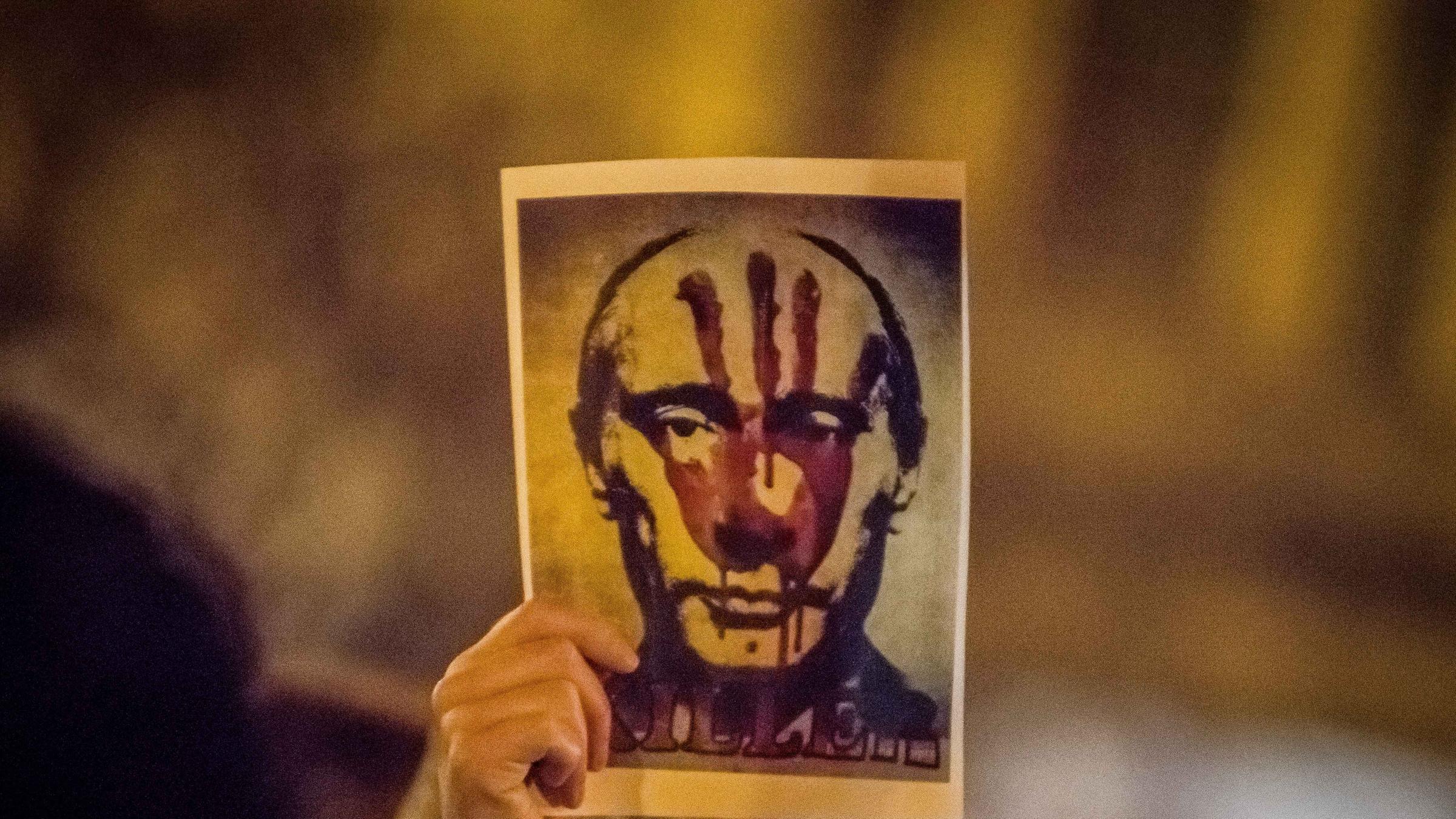 Eine Hand hält ein Bild von Putin hoch, auf dem ein blutiger Handabdruck und die Aufschrift "Killer" zu sehen ist.