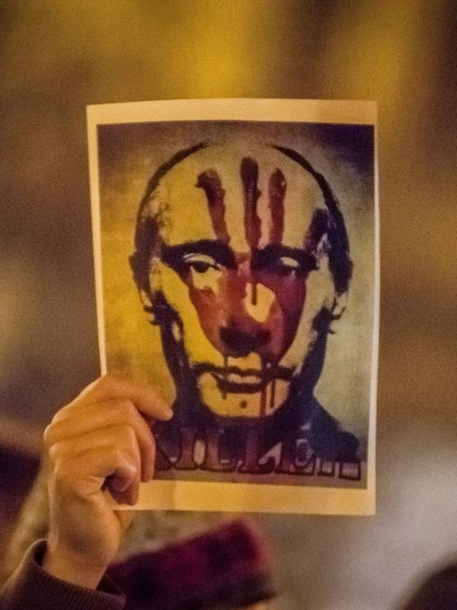 Eine Hand hält ein Bild von Putin hoch, auf dem ein blutiger Handabdruck und die Aufschrift "Killer" zu sehen ist.