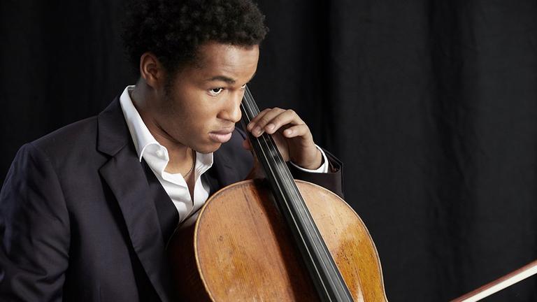 Ein junger Mann mit dunklne Locken spielt Violoncello, während sein Blick in die Ferne schweift. Ein junger Mann mit dunklne Locken spielt Violoncello, während sein Blick in die Ferne schweift.