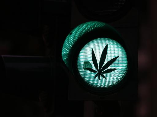 Verkehrsampel mit grünem Licht, auf das ein Aufkleber in Form einer Hanfpflanze geklebt ist.