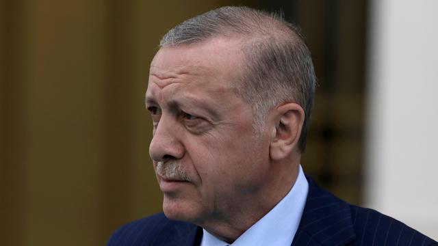 Das Bild zeigt den türkischen Präsidenten Recep Tayyip Erdogan im Porträt. Er trägt einen dunkelblauen Anzug mit einem hellblauen Hemd und schaut mit ernster Miene nach links.